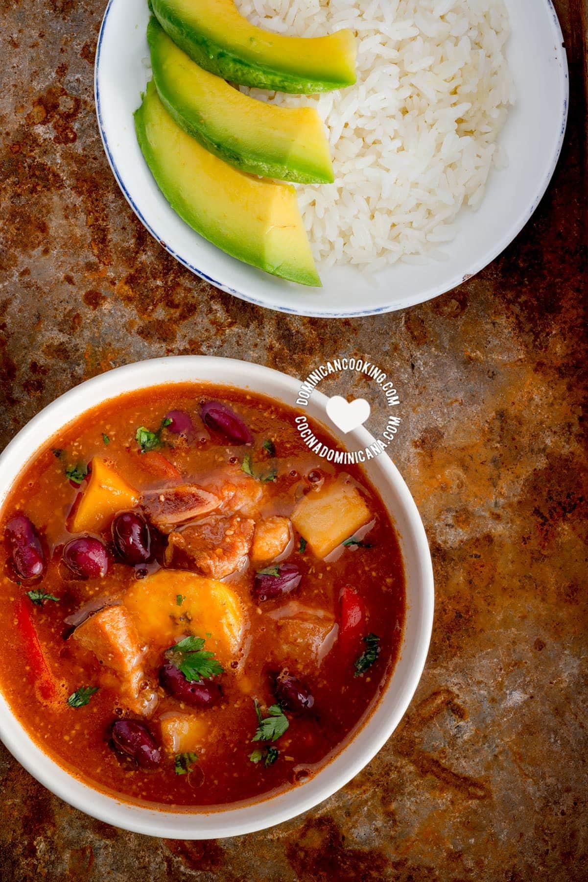 Bowl of sancocho de habichuelas or sopión or zambumbio (sweet & spicy bean stew) served with rice and avocado slices.