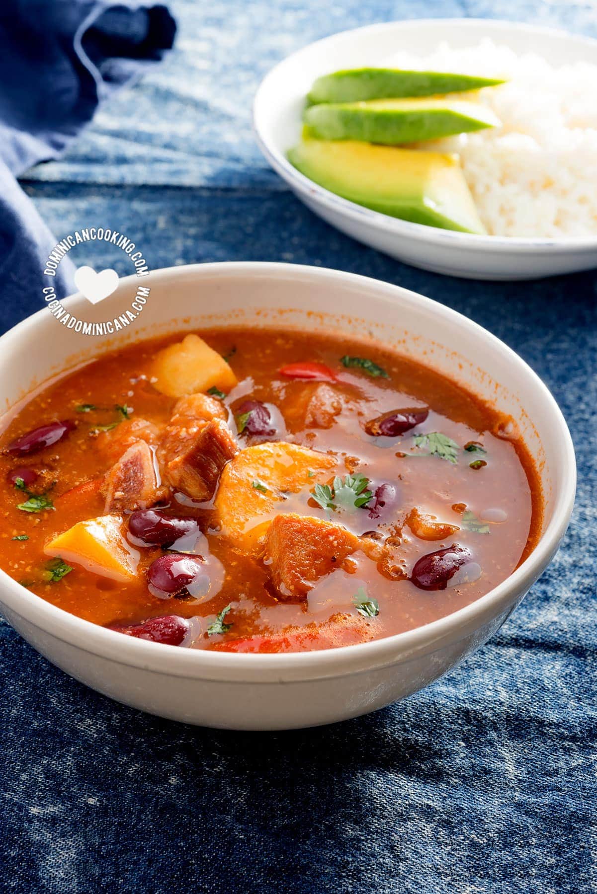 Bowl of sancocho de habichuelas or sopión or zambumbio (sweet & spicy bean stew) served with rice and avocado slices.